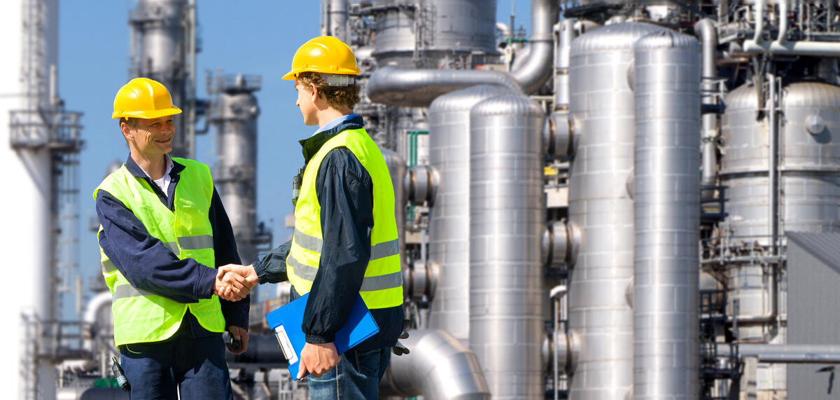 Male in a hard hat and yellow vest shakes hand with another male at a oil refinery