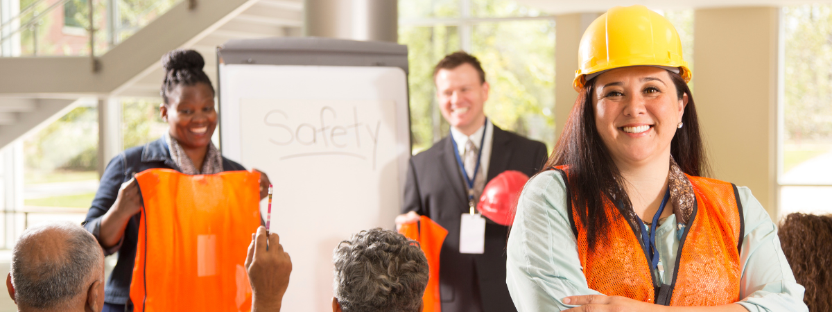 Photo of safety meeting with smiling workers in yellow hard hats and orange safety vests