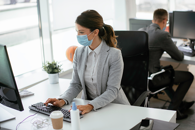 Woman working at office desk with a mask